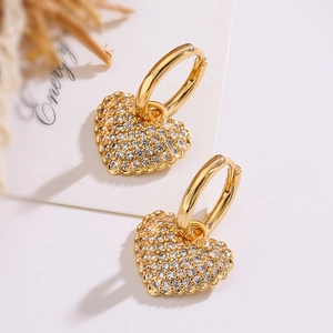 Elegant gold heart earrings with zircon crystals on a minimalist decorative background