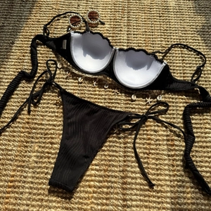 Close-up of black ribbed bikini with shell charms on a rustic straw mat background