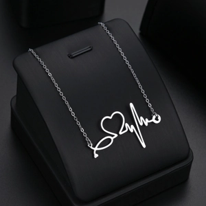 Silver stethoscope necklace with heart and EKG wave pendant on black display stand