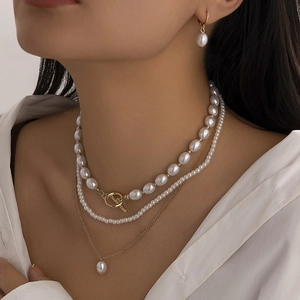 Close-up of triple-layered pearl necklace with golden OT buckle and matching drop earrings