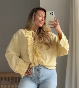 Close-up of a pale yellow chiffon blouse featuring ruffle trim and a V-neck tie detail