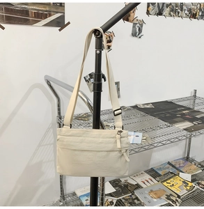 Detail of off-white nylon crossbody bag showing multiple zippers and wide strap