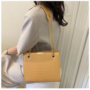 Detail of khaki crocodile pattern shoulder bag with golden chain straps on model