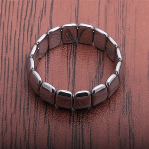 Macro detail of elastic hematite bracelet featuring square metallic beads on a brown texture