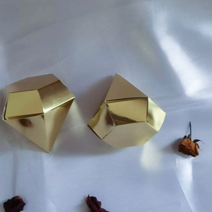 Close-up of golden diamond shaped wedding favor boxes on white silk with dried petals