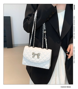 Close-up of white quilted handbag featuring a silver metal bow detail and chain strap