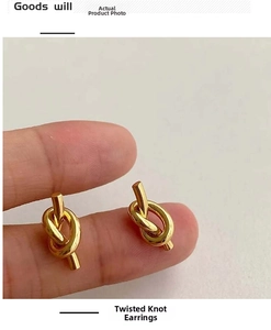 Close-up of minimalist gold knot twisted stud earrings held by hand on white backdrop