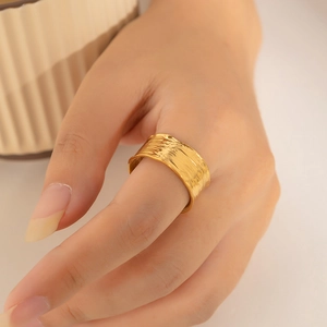 Detailed view of wide gold plated ring with hammered texture on a model's finger