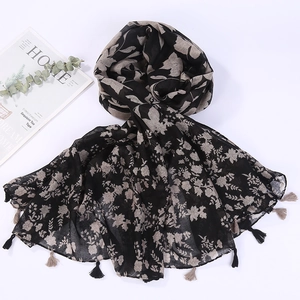 Detailed flat lay of black beach shawl with beige floral pattern and tassel edges