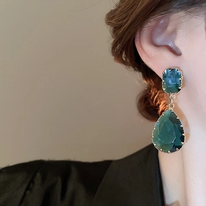 Close-up of elegant emerald green teardrop earrings with gold-plated metal claw settings