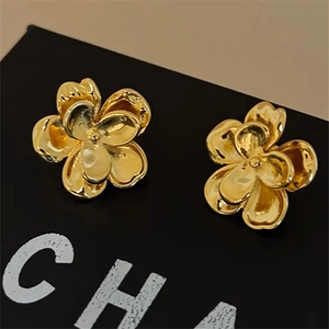 Close-up of golden metallic camellia flower stud earrings on a black gift box
