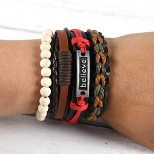 Detail of layered leather bracelet with wooden beads and engraved 'believe' metal plate
