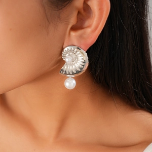 Detail of silver conch shell earring with pearls worn by a model for a beach vacation look