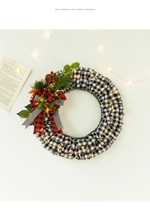 Detail of Christmas wreath with buffalo plaid, berries, pine cones and warm LED lights