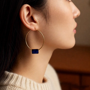 Detail view of model wearing 24k gold-plated hoop earrings with navy blue rectangular gems