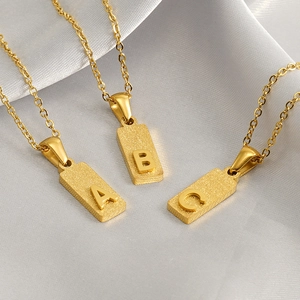 Macro view of gold rectangular alphabet pendants A, B, and C on soft silk background