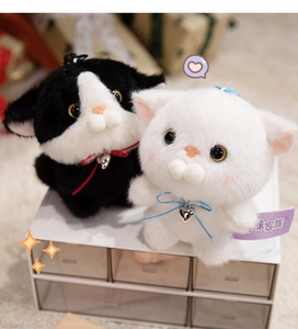 Close-up of two plush cat keychains with satin ribbons and metal heart pendants