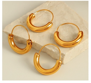 Detailed view of polished gold chunky C-shaped hoop earrings on beige stone texture