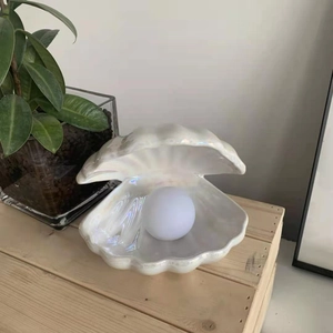 Detailed view of ceramic shell night light with glowing pearl on a rustic wooden desk