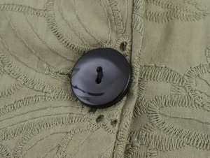 Detail of khaki green embroidery fabric with a black button and delicate eyelet texture