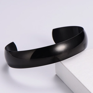 Detailed view of a sleek black mirror-finish Mobius cuff bracelet on a white geometric prop