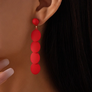 Exaggerated red geometric matte earrings with cascading oval discs worn by model