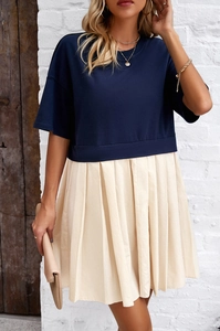 Dettaglio di un abito con top blu scuro e gonna a pieghe beige abbinata a una borsa a mano