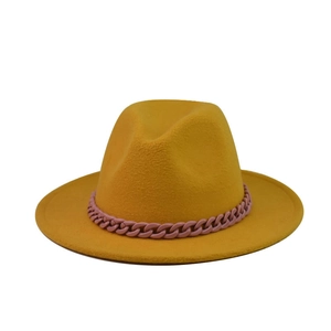 Détail d'un chapeau fedora jaune gingembre à bord large avec une chaîne décorative rose