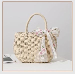 Detail of beige woven straw tote bag featuring a pink floral embroidered silk ribbon bow