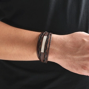 Close-up of a men's layered leather bracelet featuring brown braids and a silver metal bar