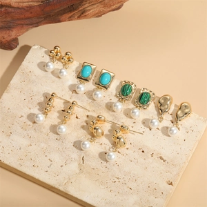 Golden earrings set with pearls and emerald malachite stones on a marble background