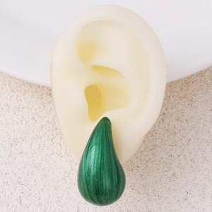 Close-up of green teardrop enamel earrings displayed on a silicone model ear