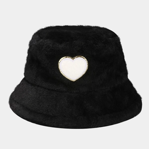 Detailed view of black faux fur bucket hat featuring a white heart patch and plush texture