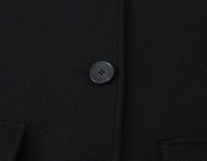 Detailed close-up of matte black four-hole button on premium wool blend fabric coat