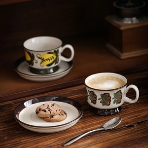 Hand-painted ceramic coffee cup and saucer set with vintage floral patterns on wooden table