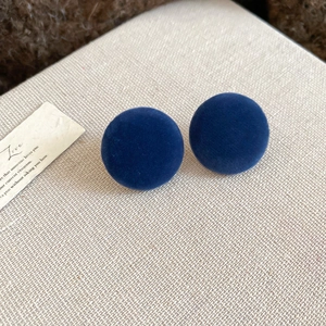Macro shot of dark blue velvet round stud earrings on a textured fabric background