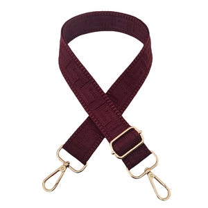 Close-up of burgundy geometric pattern bag strap with gold metal hooks and buckle