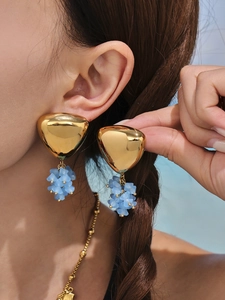 Close-up of golden triangle earrings with light blue matte floral charms on a model