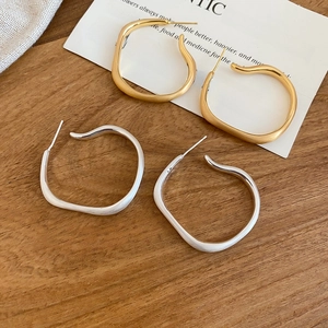 Detail view of irregular matte gold and silver hoop earrings on a wooden background