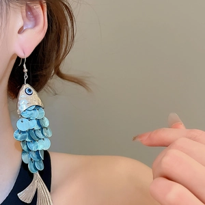 Detail view of large fish-shaped dangle earrings with blue scales and evil eye charm