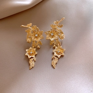 Macro shot of gold flower drop earrings with rhinestones on a silk champagne background