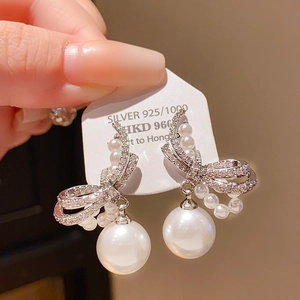 Macro shot of 925 sterling silver bow earrings with round white pearl pendants and zircons