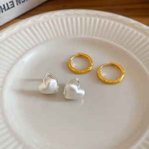 Close-up of golden hammered hoop earring and silver heart hoop on white textured plate