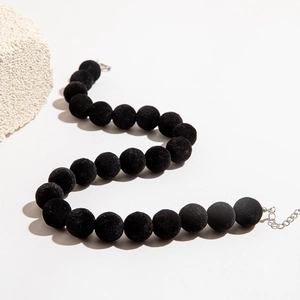 Détail d'un collier de perles floquées noires avec fermoir argenté sur fond blanc épuré
