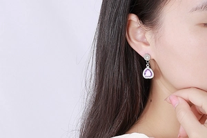 Close-up of heart-shaped purple crystal earrings with zircon halo worn by a model