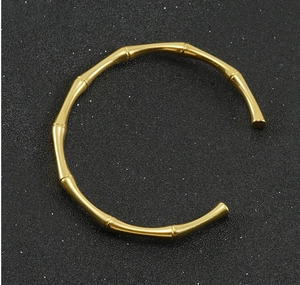 Dettaglio del bracciale rigido dorato 18K con design a bambù su fondo testurizzato