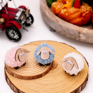 Close-up of three handmade felt sheep ornaments in pink, blue, and white for Christmas