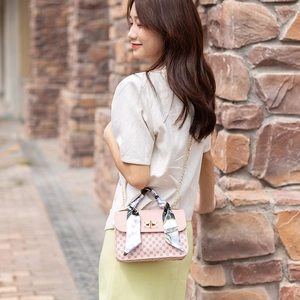 Pink crossbody bag with geometric print and silk scarf handle on an outdoor model