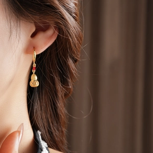 Macro shot of gold plated gourd earrings with red accent worn by model in soft light