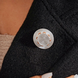 Macro shot of silver metallic woven brooch with orange details on a black blazer lapel